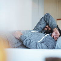 Bildet viser en ung mann som ligger på sofaen med høyre arm over hodet.