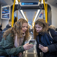 Bildet viser to unge jenter som ser på mobilene sine på trikken.