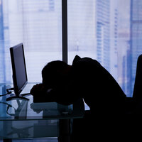Bildet viser silhuett av en mann som ligger med hodet i armene foran pc-en