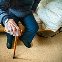 Bildet viser hånden til en gammel mann som støtter seg til en stokk.